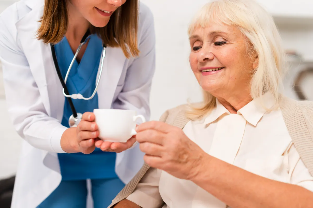 Pflegekraft reicht einer Seniorin eine Tasse Tee