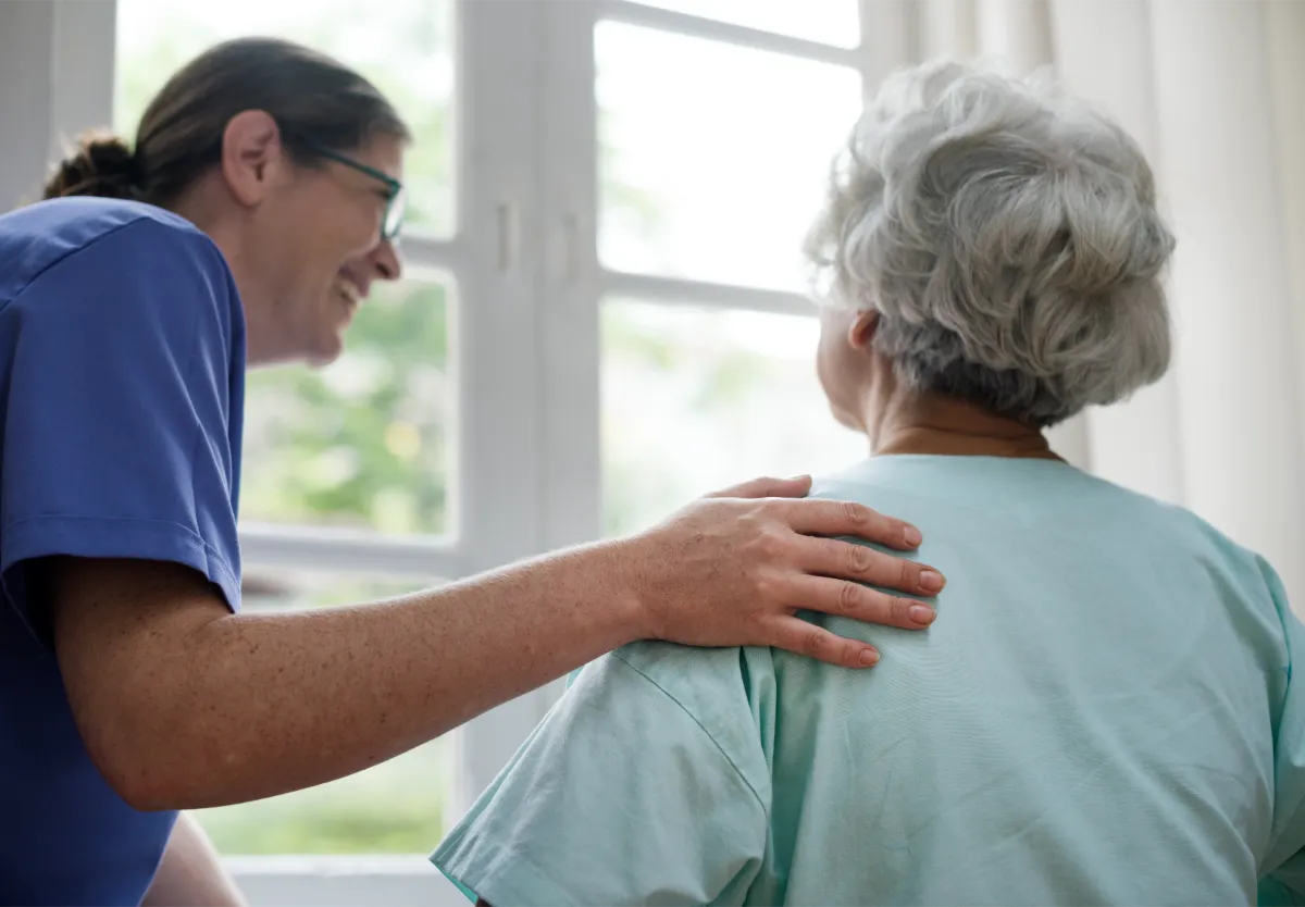 Pflegekraft unterstützt eine Seniorin beim Aufstehen